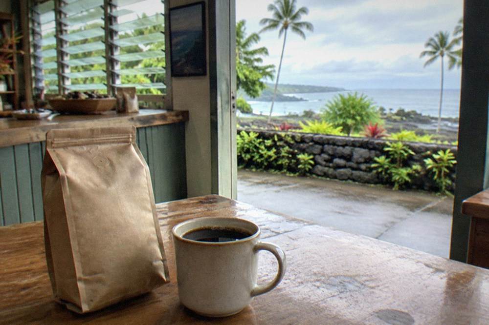 A roasted coffee bag with a percentage label beside a cup of black coffee on a wooden table