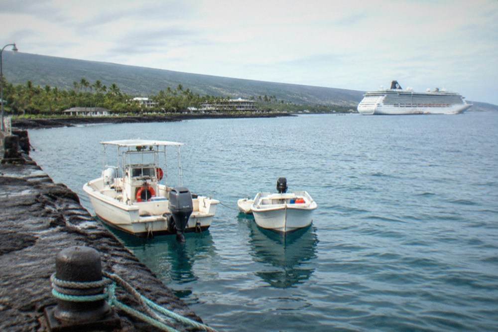 Tender boats moored at a stone pier in Kailua Kona with a cruise ship at anchor offshore
